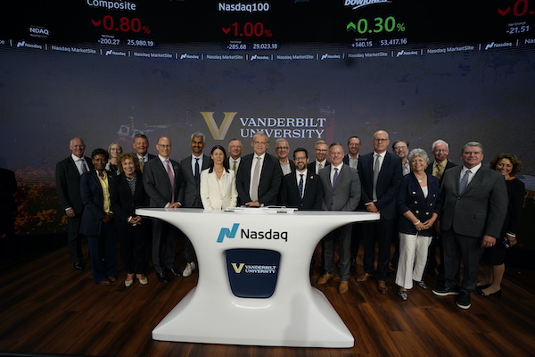 A group of professionals poses for a photo at a Nasdaq trading desk with Vanderbilt University branding, in front of a stock market display.